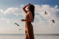 Happy asian woman with hands in the air walks on the seaside in autumn. Seagulls flying on the beach. Royalty Free Stock Photo