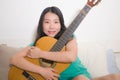 Young happy Asian woman playing guitar in bed - attractive and beautiful Chinese girl in bedroom enjoying singing and writing Royalty Free Stock Photo