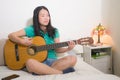 Young happy Asian woman playing guitar in bed - attractive and beautiful Chinese girl in bedroom enjoying singing and writing Royalty Free Stock Photo