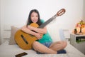 Young happy Asian woman playing guitar in bed - attractive and beautiful Chinese girl in bedroom enjoying singing and writing Royalty Free Stock Photo