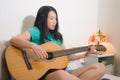Young happy Asian woman playing guitar in bed - attractive and beautiful Korean girl in bedroom enjoying singing and writing music Royalty Free Stock Photo