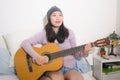 Young happy Asian woman playing guitar in bed - attractive and beautiful Korean girl in bedroom enjoying singing and writing music Royalty Free Stock Photo