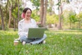 A young happy Asian woman sits on the grass in a park having a video call on her laptop Royalty Free Stock Photo