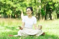 Young happy asian woman sitting on grass at park ,wearing earphones listening to music relaxing with coffee .Nature essential