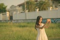 Young happy Asian woman smiling while taking selfie picture with mobile phone against grass field and fancy house Royalty Free Stock Photo