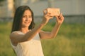 Young happy Asian woman smiling while taking selfie picture with mobile phone against grass field Royalty Free Stock Photo