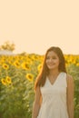 Young happy Asian woman smiling and thinking in the field of blooming sunflowers Royalty Free Stock Photo