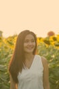 Young happy Asian woman smiling and thinking while looking at distance in the field of blooming sunflowers Royalty Free Stock Photo