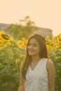 Young happy Asian woman smiling and thinking while looking at distance in the field of blooming sunflowers Royalty Free Stock Photo