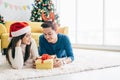 Young happy Asian woman wearing a Santa Claus hat with her boyfriend with a Christmas gift while lying down on the carpet. Royalty Free Stock Photo