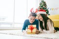 Young happy Asian woman wearing a Santa Claus hat with her boyfriend with a Christmas gift while lying down on the carpet. Royalty Free Stock Photo