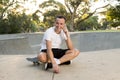 Young happy and attractive American man 30s sitting on skate board after sport boarding training session talking on mobile phone Royalty Free Stock Photo