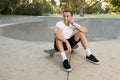 Young happy and attractive American man 30s sitting on skate board after sport boarding training session talking on mobile phone Royalty Free Stock Photo