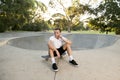 Young happy and attractive American man 30s sitting on skate board after sport boarding training session talking on mobile phone Royalty Free Stock Photo