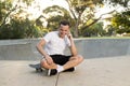 Young happy and attractive American man 30s sitting on skate board after sport boarding training session talking on mobile phone Royalty Free Stock Photo