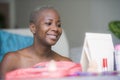 Young happy and attractive black african American woman wrapped in towel applying makeup cosmetics looking and smiling to herself Royalty Free Stock Photo