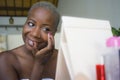 Young happy and attractive black african American woman wrapped in towel applying makeup cosmetics using fingers putting base prim Royalty Free Stock Photo