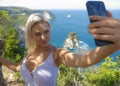 Young happy and attractive blond woman taking selfie portrait with mobile phone at beautiful tropical paradise view of ocean rock Royalty Free Stock Photo