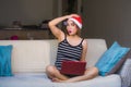 Young happy and attractive girl relaxed at apartment couch in Santa Claus hat using laptop computer buying Christmas present smili Royalty Free Stock Photo