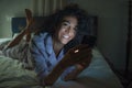 Young happy and attractive hipster woman cozy on bed at night enjoying internet social media app on mobile phone online dating and Royalty Free Stock Photo