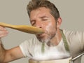 Young happy and attractive home cook man in apron cheerful and charming tasting stew with spoon isolated on even background