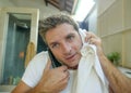 Young happy and attractive man drying with towel after washing face at home bathroom mirror while speaking on the mobile phone smi Royalty Free Stock Photo