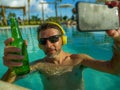 Young happy and attractive man taking selfie picture with mobile phone drinking beer and listening to music at tropical resort Royalty Free Stock Photo