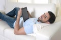 Young happy attractive man using digital pad or tablet sitting on couch Royalty Free Stock Photo