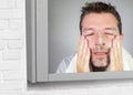 Young happy attractive man washing face with anti aging soap lotion smiling confident and conscious looking at bathroom mirror in Royalty Free Stock Photo