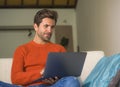 Young happy and attractive man working relaxed with laptop computer at modern apartment living room sitting at sofa couch typing a Royalty Free Stock Photo