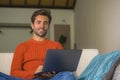 Young happy and attractive man working relaxed with laptop computer at modern apartment living room sitting at sofa couch typing a Royalty Free Stock Photo