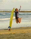 Young happy and attractive surfer girl jumping high in the air holding surf board before surfing at beautiful tropical beach enjoy Royalty Free Stock Photo