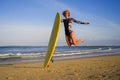 Young happy and attractive surfer girl jumping high in the air holding surf board before surfing at beautiful tropical beach enjoy Royalty Free Stock Photo