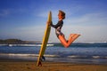 Young happy and attractive surfer girl jumping high in the air holding surf board before surfing at beautiful tropical beach enjoy Royalty Free Stock Photo