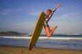 Young happy and attractive surfer girl jumping high in the air holding surf board before surfing at beautiful tropical beach enjoy Royalty Free Stock Photo