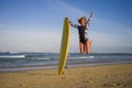 Young happy and attractive surfer girl jumping high in the air holding surf board before surfing at beautiful tropical beach enjoy Royalty Free Stock Photo