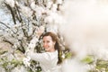 Young happy attractive woman in light casual clothes kepping hand near branches with flowers standing in city garden or