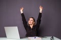 Young happy attractive woman at modern office desk, with laptop feeling with raised hands of celebreting cheerful good morning new