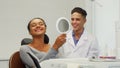 Beautiful woman checking her smile in the mirror at the dental clinic