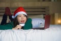 Young happy and beautiful Asian American girl on bed in Santa Christmas hat using credit card and laptop computer for online shopp Royalty Free Stock Photo