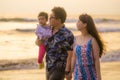 Young happy and beautiful Asian Chinese couple holding baby girl daughter walking on sunset beach enjoying together romantic Royalty Free Stock Photo
