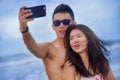 young happy and beautiful Asian Chinese couple taking selfie photo with mobile phone camera smiling joyful having fun on the beach Royalty Free Stock Photo