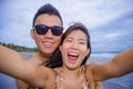 young happy and beautiful Asian Chinese couple taking selfie photo with mobile phone camera smiling joyful having fun on the beach Royalty Free Stock Photo