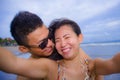 young happy and beautiful Asian Chinese couple taking selfie photo with mobile phone camera smiling joyful having fun on the beach Royalty Free Stock Photo