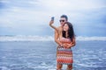 young happy and beautiful Asian Chinese couple taking selfie photo with mobile phone camera smiling joyful having fun on the beach Royalty Free Stock Photo