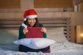 Young happy and beautiful Asian Chinese woman on bed in Santa Christmas hat using credit card and laptop computer for online shopp Royalty Free Stock Photo