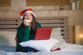 Young happy and beautiful Asian Chinese woman on bed in Santa Christmas hat using credit card and laptop computer for online shopp Royalty Free Stock Photo