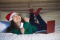 Young happy and beautiful Asian Chinese woman on bed in Santa Christmas hat using credit card and laptop computer for online shopp Royalty Free Stock Photo