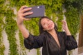 Young happy and beautiful Asian Chinese woman enjoying outdoors taking selfie with mobile phone at village garden playful and Royalty Free Stock Photo