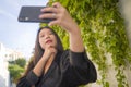 Young happy and beautiful Asian Chinese woman enjoying outdoors taking selfie with mobile phone at village garden playful and Royalty Free Stock Photo